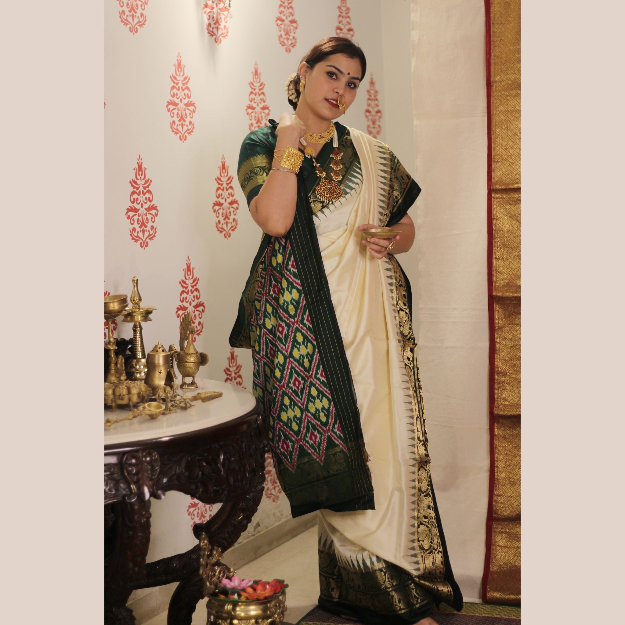 Woman in traditional attire standing in a decorated room with ornate wall patterns.