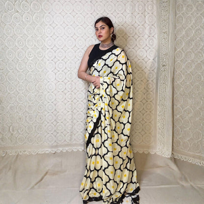Woman wearing a black and white floral saree against a white textured wall.