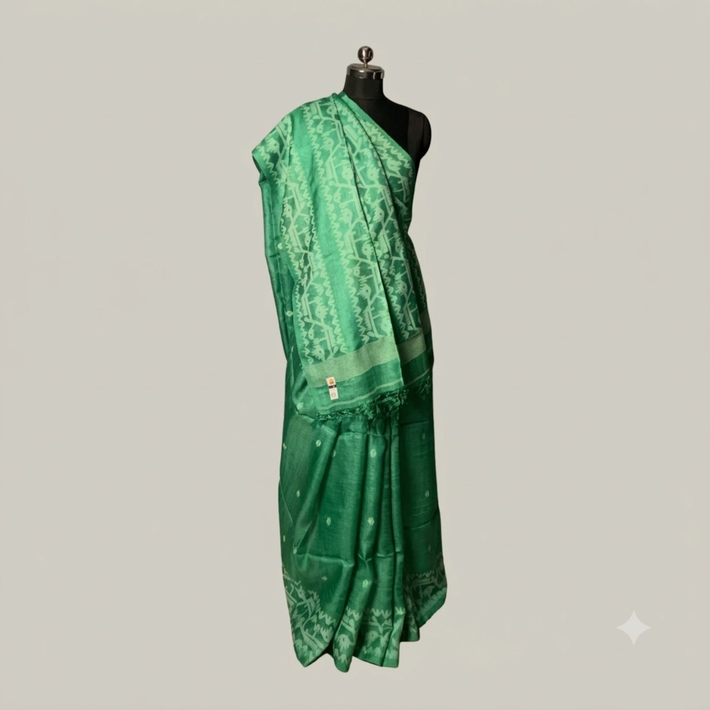A green silk saree with geometric patterns and a matching border, draped on a black mannequin torso against a solid light gray background.