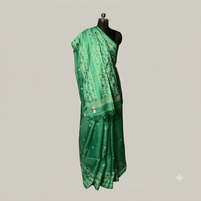 A green silk saree with geometric patterns and a matching border, draped on a black mannequin torso against a solid light gray background.