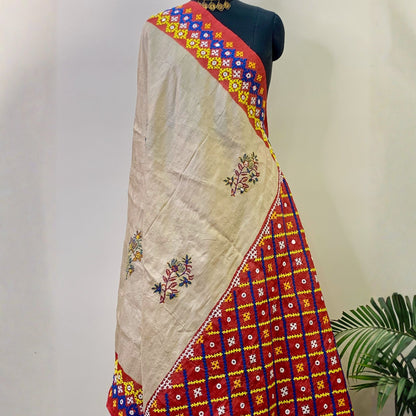 A beige silk saree draped on a black mannequin torso, featuring red, blue, and yellow borders with floral and geometric patterns, and small embroidered motifs on the body.