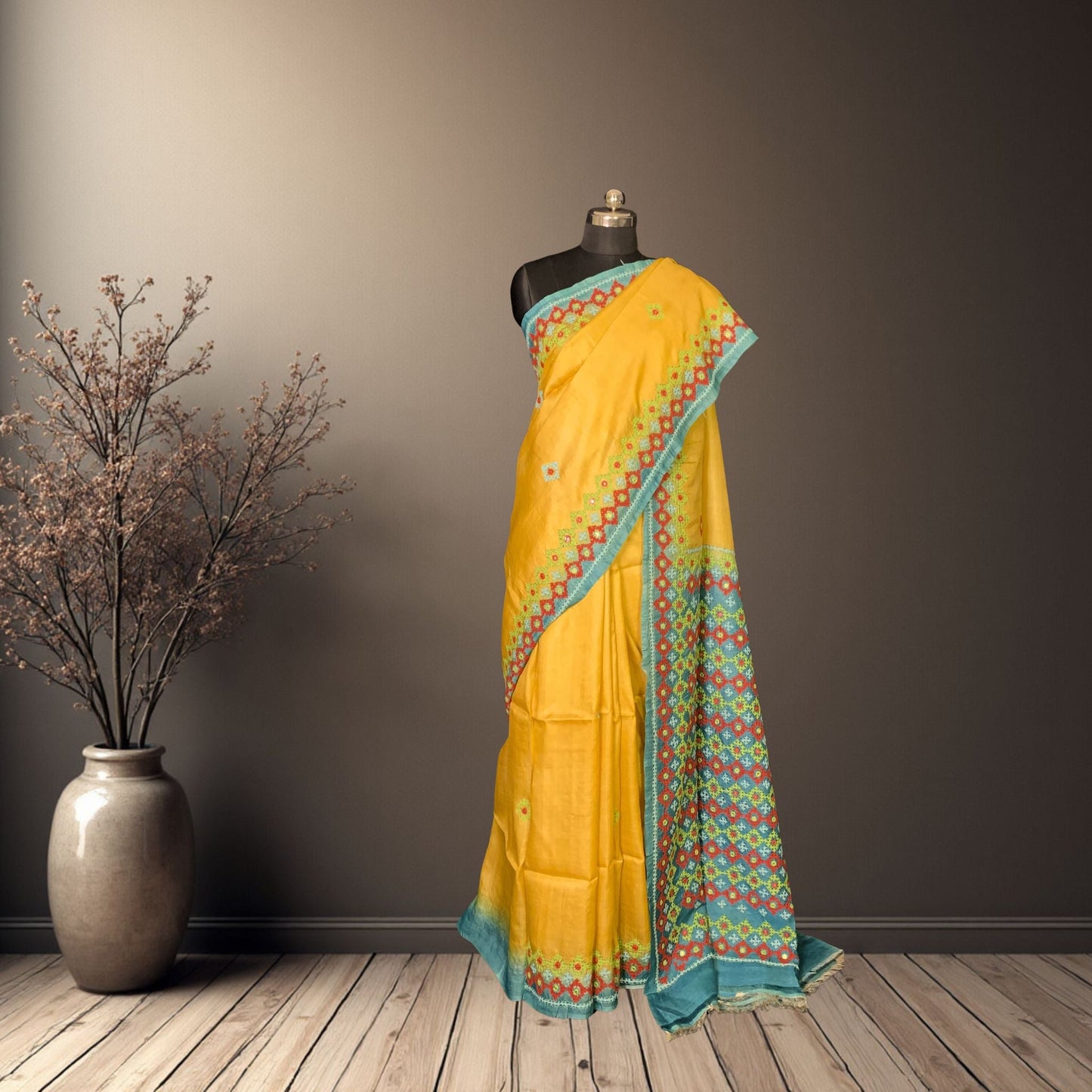 Yellow saree with blue border on a mannequin against a gray wall.