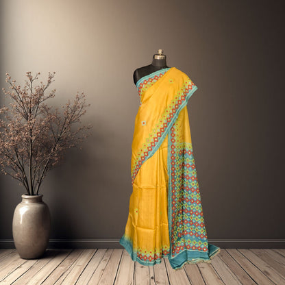 Yellow saree with blue border on a mannequin against a gray wall.