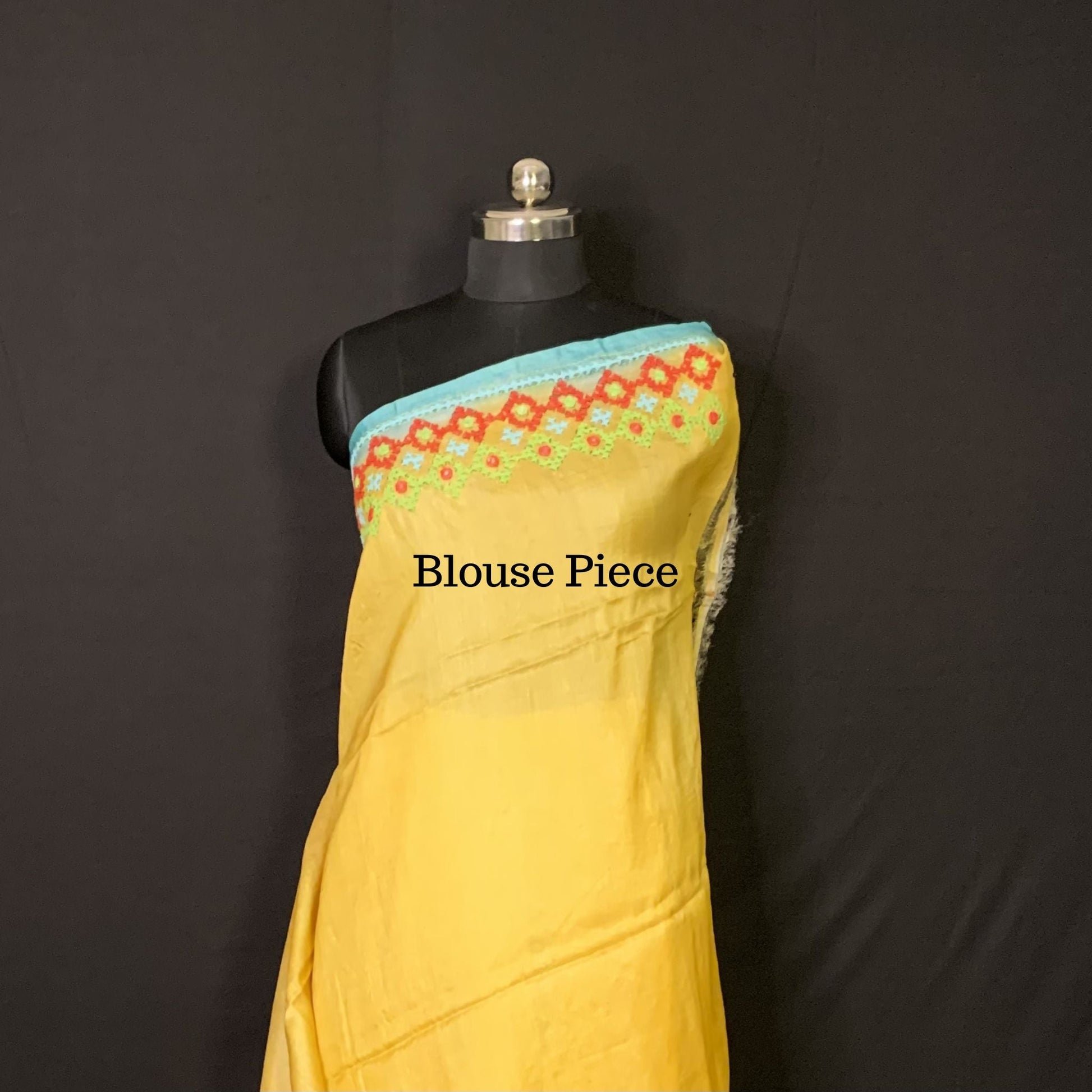 Yellow blouse piece with floral embroidery on a black mannequin against a dark background