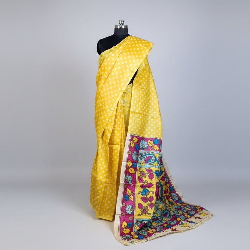 A yellow Tussar silk saree with white polka dots and a highly detailed multicolor border, displayed on a black dress form mannequin against a light gray background.